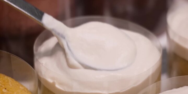 close-up shot capturing a perfectly formed, fluffy dollop of fresh whipped cream topping a rich sponge cake or mousse dessert. The camera focuses on the smooth, airy texture of the meringue cream cont