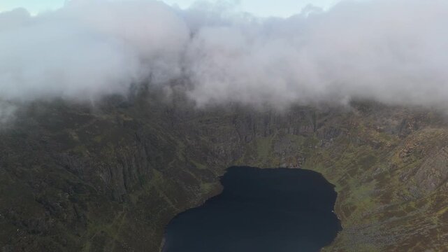 High angle view of Coumshingaun Lough tarn lake surrounded by steep cliffs and low clouds in Comeragh Mountains, County Waterford, Ireland