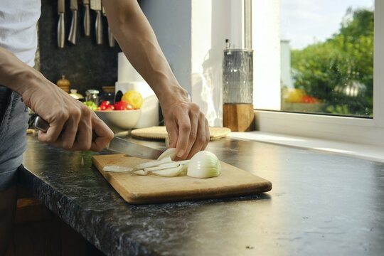 Close-up view of female hands cutting onions on cutting board on countertop near window. Option to extend windowsill to increase working space in small kitchen
