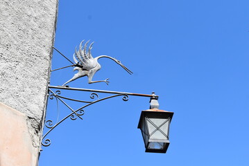 Lampadaire mural sur une façade à Gruyère. Il est orné d'une grue, animal emblème de la ville. © Valentin