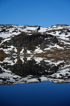 Mountain lake surrounded by rocky highland terrain and lingering snow in the Norwegian mountains.