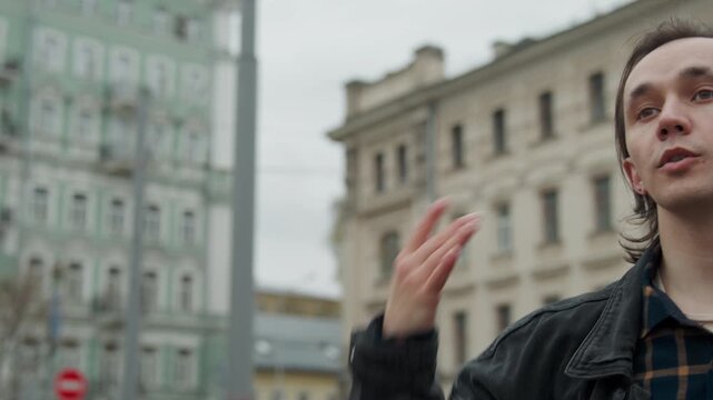 Close up of two people outdoors one with bandaged hand and other partially visible. man gestures while speaking in urban setting with historic buildings and bare trees in soft daylight. Both