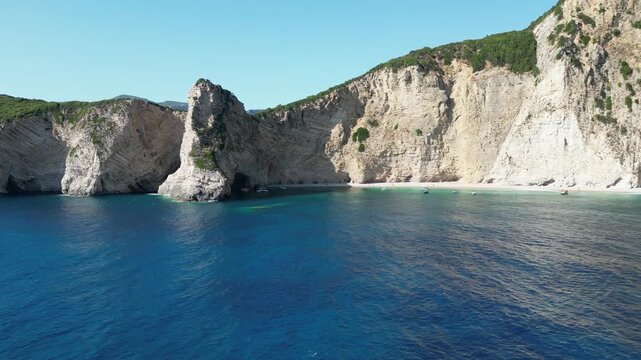 Aerial descent revealing turquoise water and bright white cliffs at Chomi Beach near Paleokastritsa