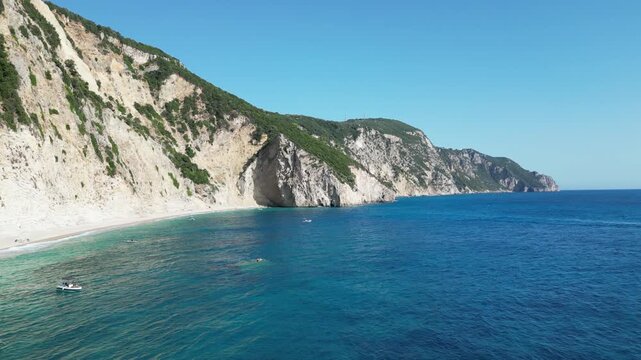 Aerial take‑off shot showing turquoise sea and white cliffs at Chomi Beach in Corfu near Paleokastritsa with a boat passing by