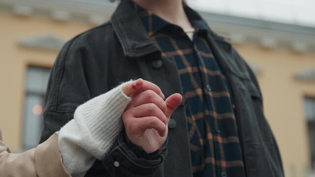 Close up of two people holding hands one with bandaged finger and wearing white knit glove. scene shows gentle interaction between people in outdoor urban environment with soft focus