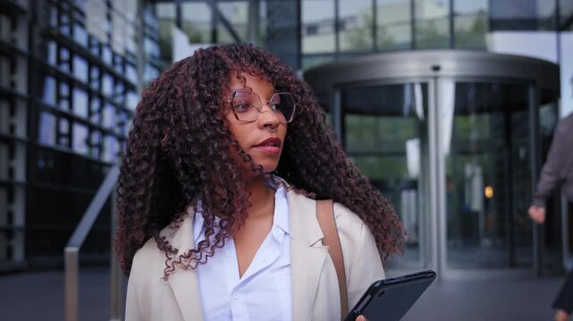 Black Latina professional leaving a modern office while passing other employees near the entrance. Candid corporate scene showing commuting, diversity and everyday workplace life.