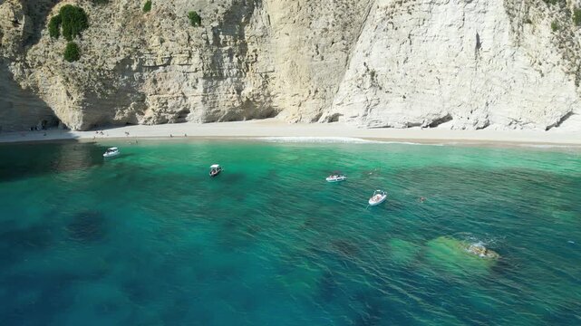 Aerial reverse shot showing turquoise sea and white cliffs at Chomi Beach in Corfu near Paleokastritsa with a boat passing by