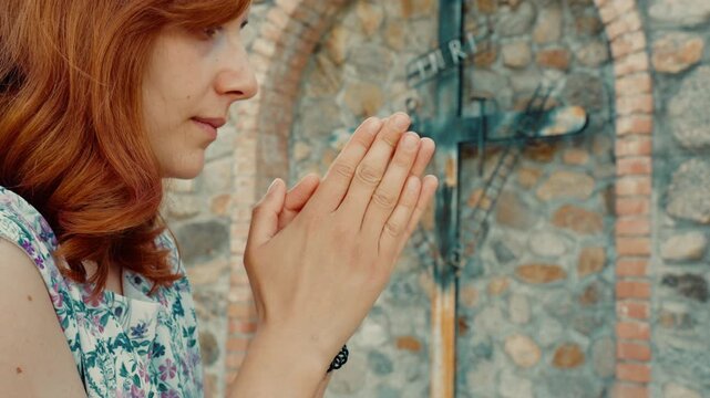 Woman prays for Jesus and the sick with her hand clasped near Christian crucifix