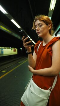 Woman scrolls through her phone while patiently waiting for the subway train