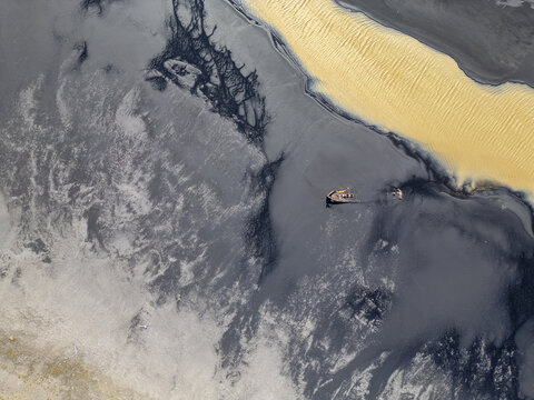 Aerial view of a glacial river with vibrant yellow water flowing through dark volcanic sand deposits in Iceland.