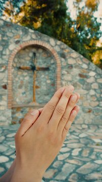Praying hands of a Christian woman in front of an outdoor crucifix