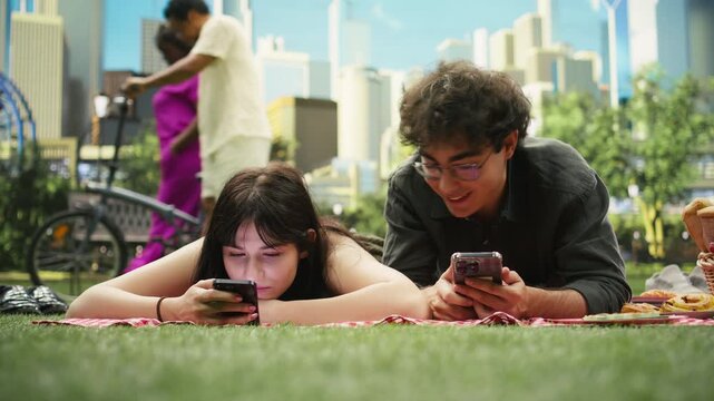 Young couple lies side by side illustrating phubbing and phone addiction on a picnic blanket, focused on separate smartphones instead of each other, showing emotional distance and no communication.
