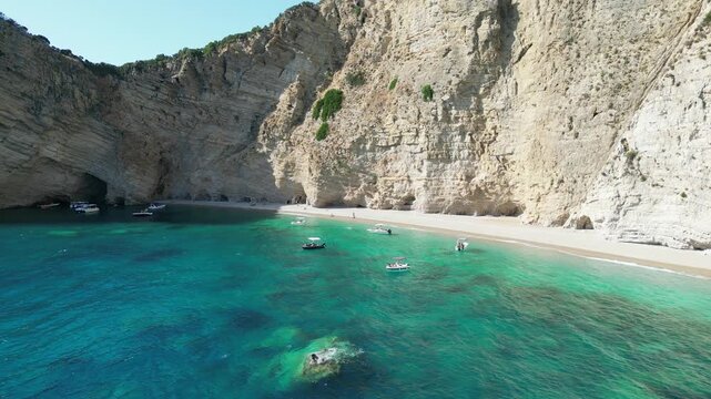 4K Aerial static shot of Chomi Beach with turquoise water, anchored boats, and white cliffs near Paleokastritsa, Corfu, Greece
