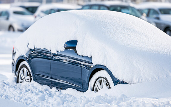 Blue car buried under heavy snowfall in winter parking lot