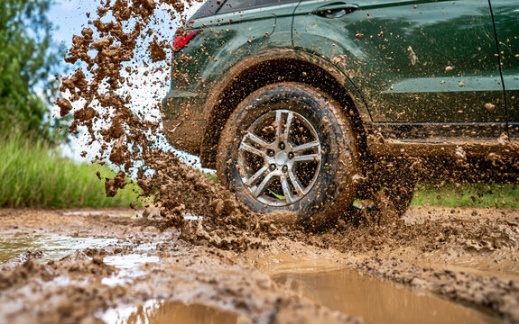 Low angle view of suv wheel driving through mud puddle on country road