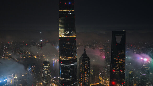 Aerial view of Lujiazui skyline at night, featuring Shanghai Tower and Shanghai World Financial Center illuminated amidst low-hanging clouds and city lights in Shanghai, Shanghai, China.