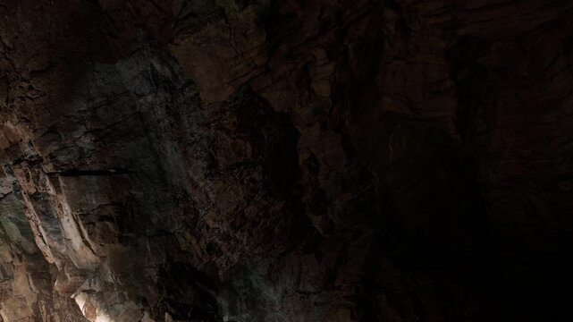 A group of people navigates through a dark cave filled with various rock formations. Lights illuminate the walls, creating shadows and enhancing the experience of exploration.