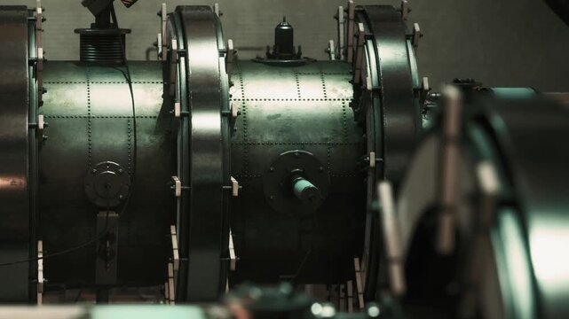 The scene shows a section of large industrial machinery in a manufacturing facility. The equipment has metallic surfaces and various pipes attached. It looks functional and busy.