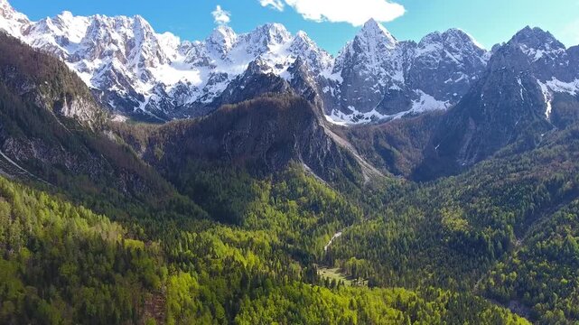 Aerial view of Triglav mountain peak rising above dense green forests under a clear blue sky in Mojstrana, Jesenice, Slovenia.