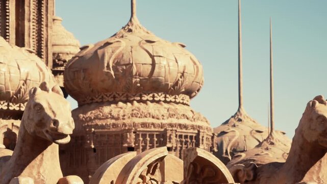 The image shows a close up view of a desert structure featuring carved sculptures and designs. The sun shines down on the surface, highlighting intricate patterns and shapes.