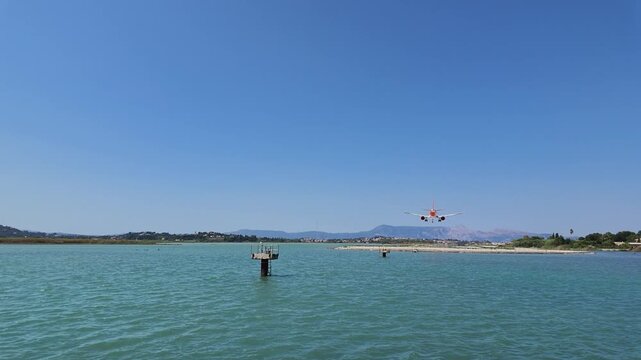4K shot showing easyJet plane flying low over the causeway near the Greek Orthodox church at Corfu Airport with a female waving