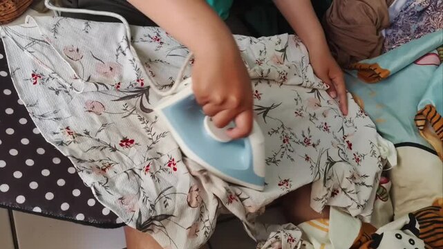 Close-up of a person ironing a floral patterned shirt on a polka dot board. Housework, chores, and daily routine clothing care concept.
