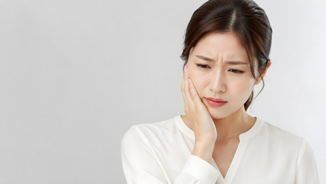 歯の痛みで頬を押さえる若い日本人女性のクローズアップ
