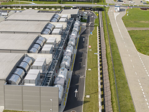 Aerial view of an AI data center power generator system with industrial tanks and cooling units next to a secure perimeter fence and paved access road in Poland.