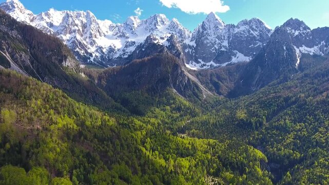 Aerial view of the snow-capped Triglav mountain range rising above the lush green forests of the Julian Alps in Mojstrana, Jesenice, Slovenia.