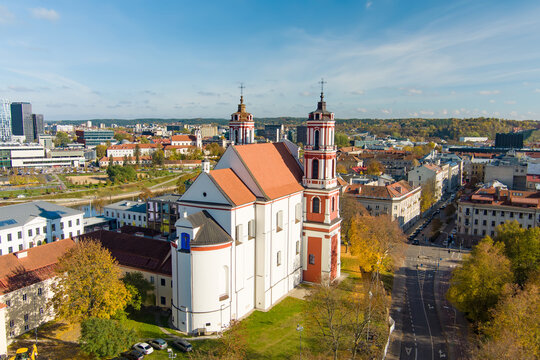 Aerial view of the Church of St. James and St. Philip surrounded by historic and modern architecture in Vilnius, Lithuania on a sunny autumn day. Twin towers rise above the city center.