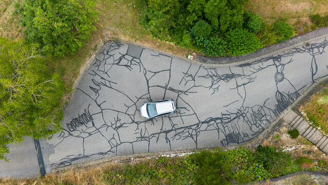 Aerial view of a silver car parked on an asphalt road with extensive cracks and dark tar patches in Trier, Rhineland-Palatinate, Germany.