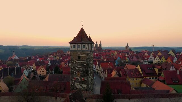 4K scenic view of Rothenburg ob der Tauber at sunset, featuring a historic medieval tower, fortified city walls, colorful houses and red tiled rooftops.