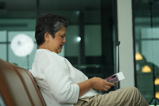 A mature female traveller in a white blouse dozes off with her hand on the luggage handle in a bright airport waiting hall, staying in touch with family while abroad