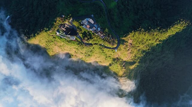 Aerial view of Mount Telomoyo via Dalangan with winding mountain roads and lush green slopes surrounded by clouds in Kecamatan Ngablak, Jawa Tengah, Indonesia.