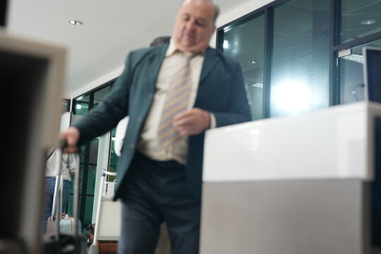 A mature passenger leaning on his trolley case hands a passport across the check in desk in the departure hall of a modern airport, with passports changing hands
