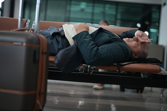 An exhausted traveller asleep on a bench dozes on the airport seats with his jacket on in the waiting area of a modern terminal, showing what a long delay really looks like