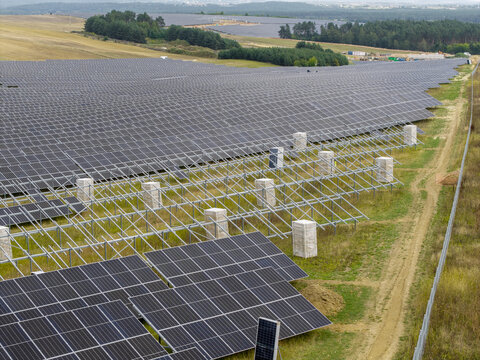 Aerial view of a large photovoltaic farm under construction with rows of solar panels mounted on metal frames in a rural landscape in Tokarnia, Swietokrzyskie Voivod, Poland.