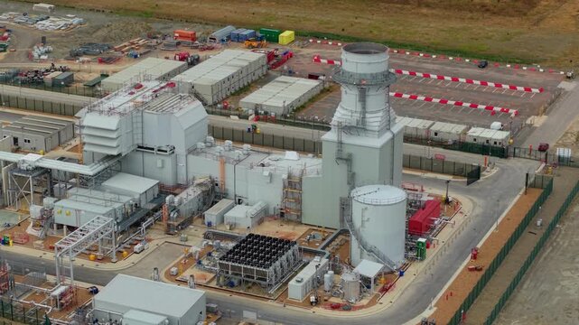 Aerial view of the Millbrook Power Plant featuring industrial buildings, a tall exhaust stack, storage tanks, and cooling equipment in Stewartby, England, United Kingdom.