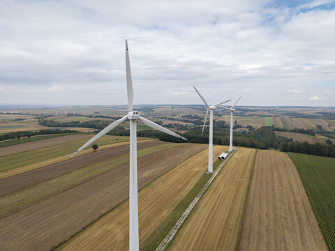 Aerial view of wind turbines standing in vast agricultural fields under a cloudy sky in Poland.