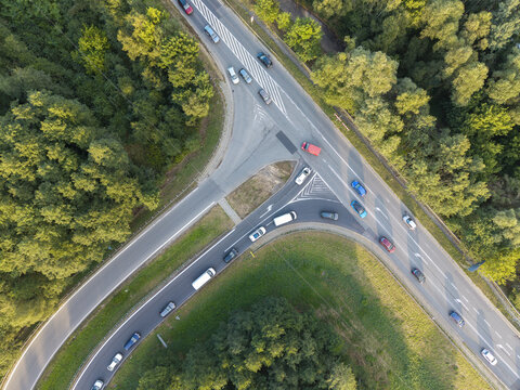 Aerial view of a highway junction with cars driving on asphalt roads surrounded by dense green forest in Krakow, Lesser Poland Voivode, Poland.