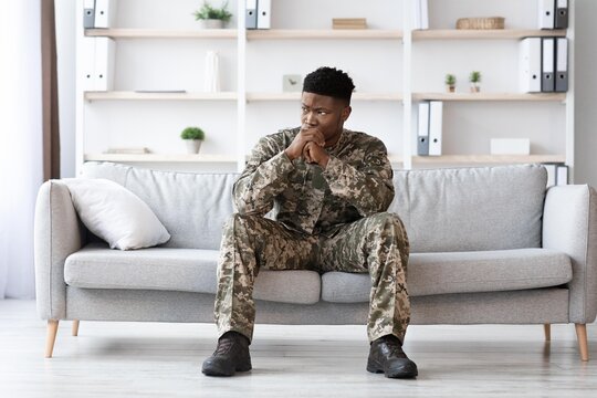 Worried Black Male Soldier In Military Uniform Sitting Thoughtfully On Couch At Home, Reflecting On Experiences And Emotions, Creating A Sense Of Calmness And Introspection. Military Concept.
