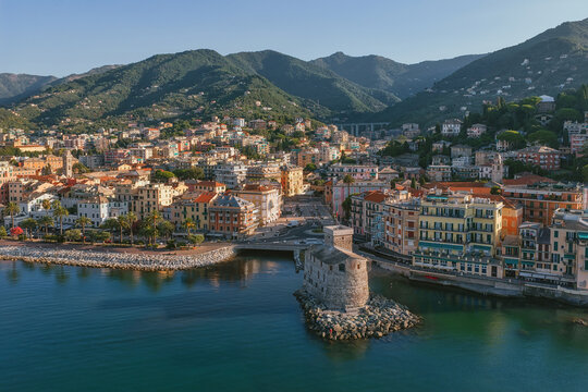 Aerial view of the historic Castello di Rapallo situated on the coast with colorful buildings, lush green hills, and the Mediterranean Sea in Rapallo, Liguria, Italy.