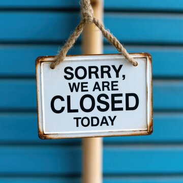 White metal sign with sorry we are closed today hanging from a rope against blue wall