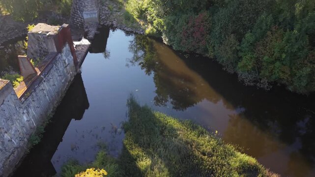 Aerial view of the historic Yngeredsfors powerplant ruins at Doda Fallet, featuring stone walls and calm river water surrounded by lush forest in Vessigebro, Hallands lan, Sweden.