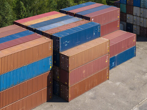 Aerial view of stacked shipping containers at an e-commerce logistics terminal with vibrant red, blue, and orange metal units arranged in rows on a paved yard in Poland.