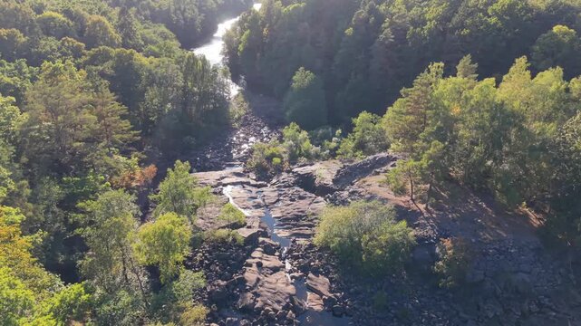 Aerial view of the historic Yngeredsfors Doda Fallet powerplant site, featuring rocky riverbeds, lush green forest, and flowing water in Vessigebro, Hallands lan, Sweden.