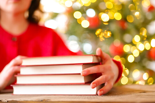 Holiday Reading and Learning with Books at Christmas.Woman Reading Books During Christmas Winter Holidays.hardcover books beside a glowing Christmas tree for bookstore advertising, library events