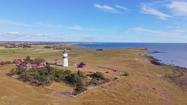 Aerial view of Morups Tange lighthouse surrounded by red wooden houses and coastal fields in Glommen, Hallands lan, Sweden.