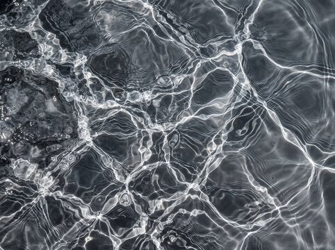 Abstract water surface texture showing ripples and caustic light patterns reflecting in shades of grey with light reflec