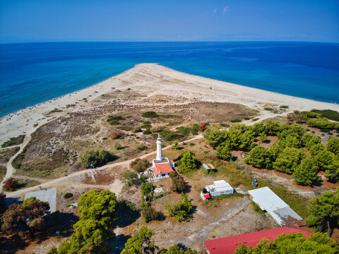 Aerial view of the historic Possidi Lighthouse situated on a sandy cape surrounded by turquoise Aegean Sea waters and pine forests in Possidi, Greece.